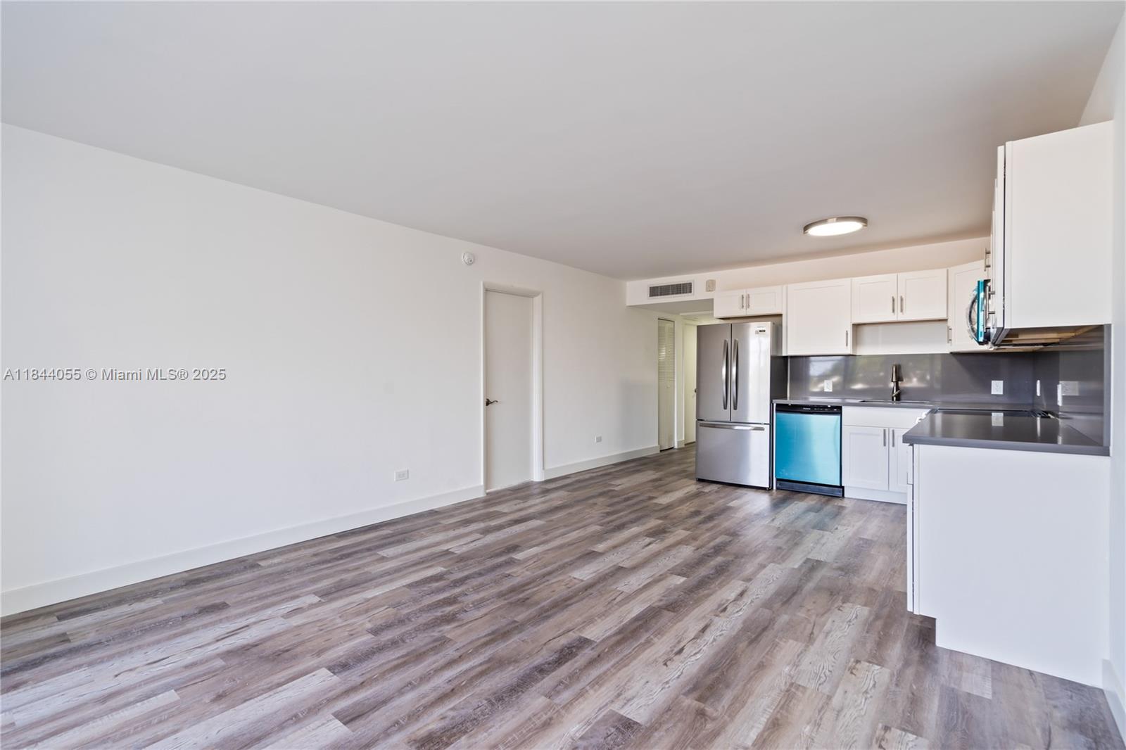 An open-concept kitchen and living area features white cabinetry, stainless steel appliances, and wood-look flooring — 445 NE 195th St # 330, Miami FL 33179, MIAMI, FL