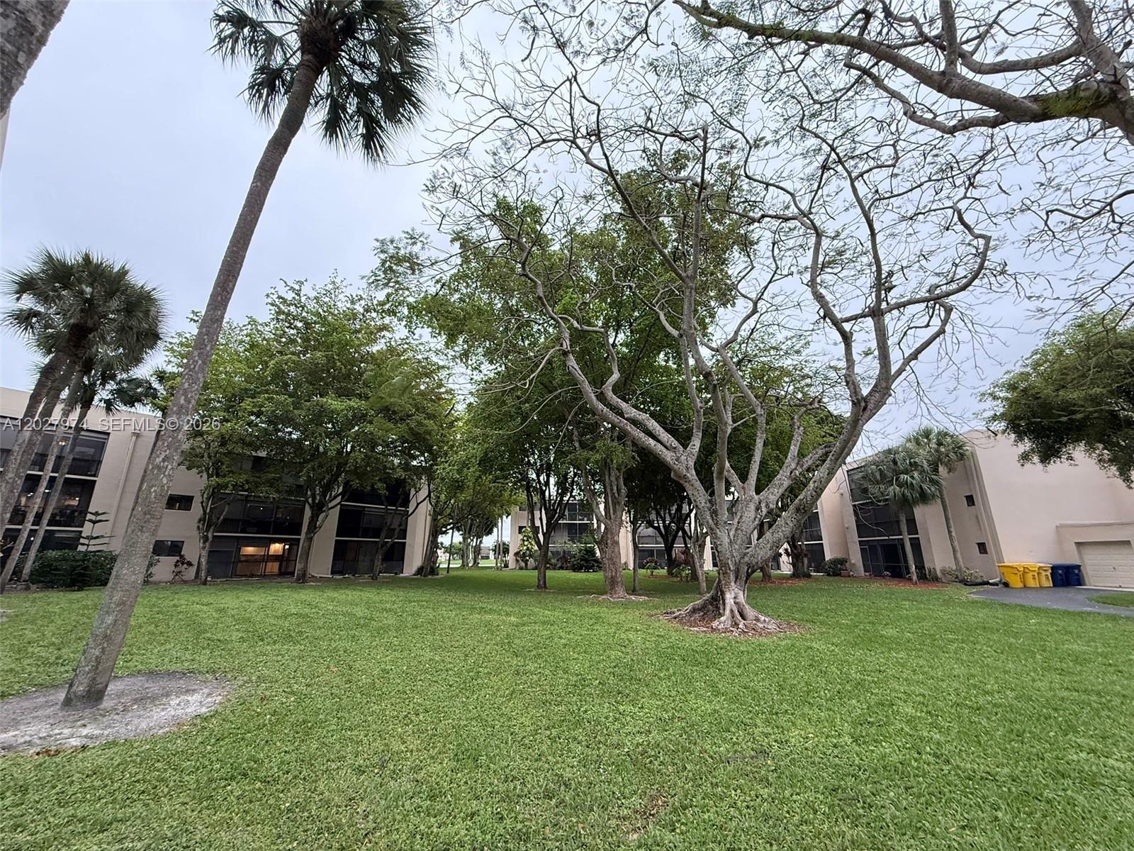 A grassy courtyard sits between multi-story apartment buildings surrounded by various trees and palms — 5220 Las Verdes Cir # 114, Delray Beach FL 33484, DELRAY BEACH, FL