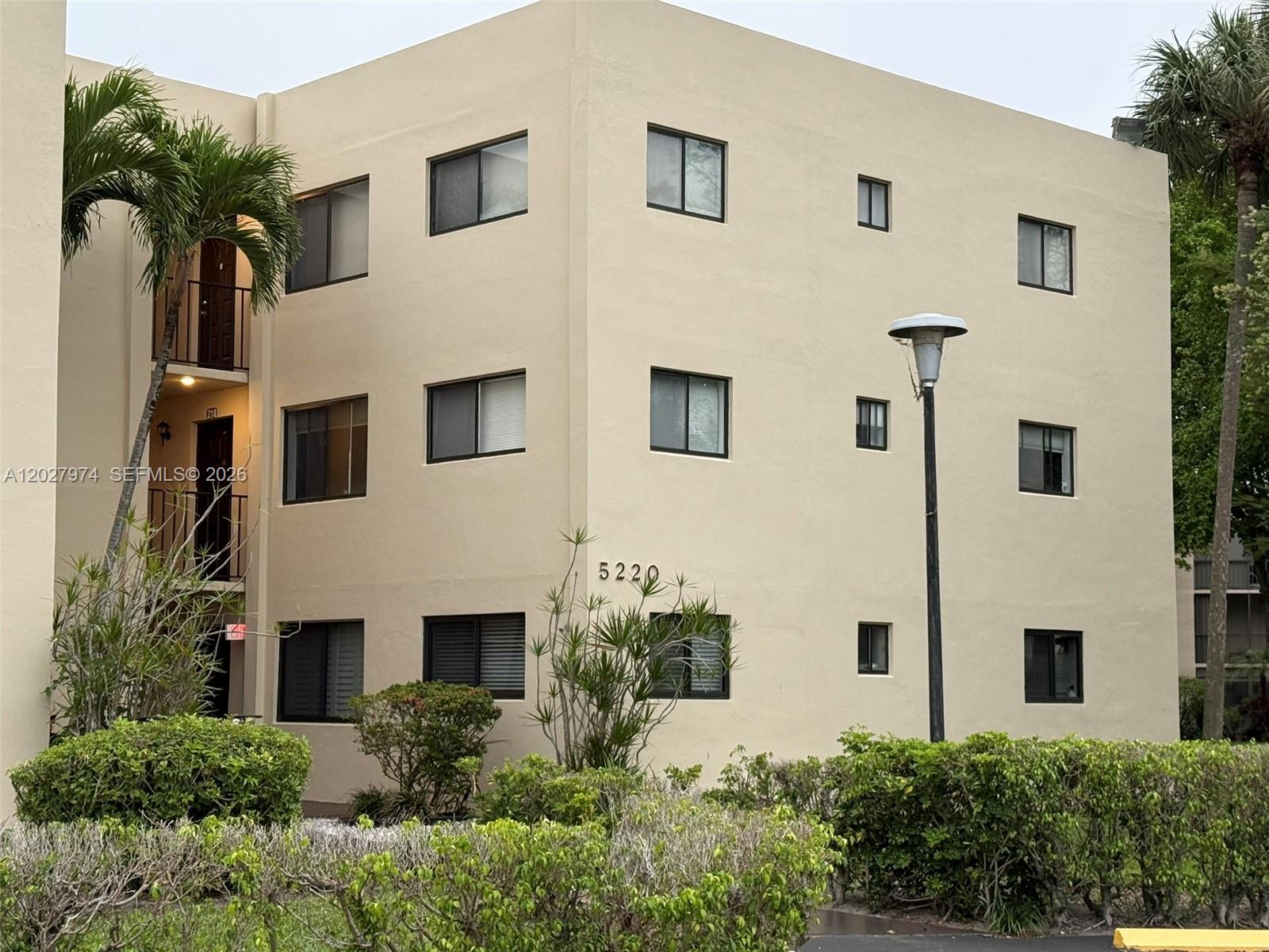 A three-story tan apartment building features dark-framed windows and a palm tree in front — 5220 Las Verdes Cir # 114, Delray Beach FL 33484, DELRAY BEACH, FL