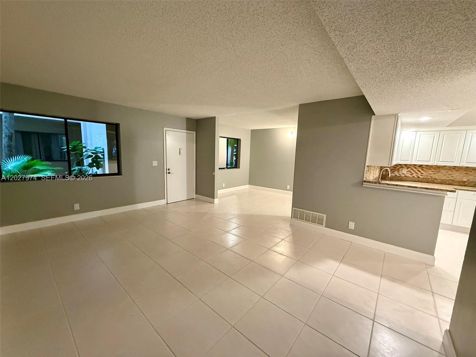 An open-concept living area features light-colored tile flooring, gray walls, and an adjacent kitchen — 5220 Las Verdes Cir # 114, Delray Beach FL 33484, DELRAY BEACH, FL