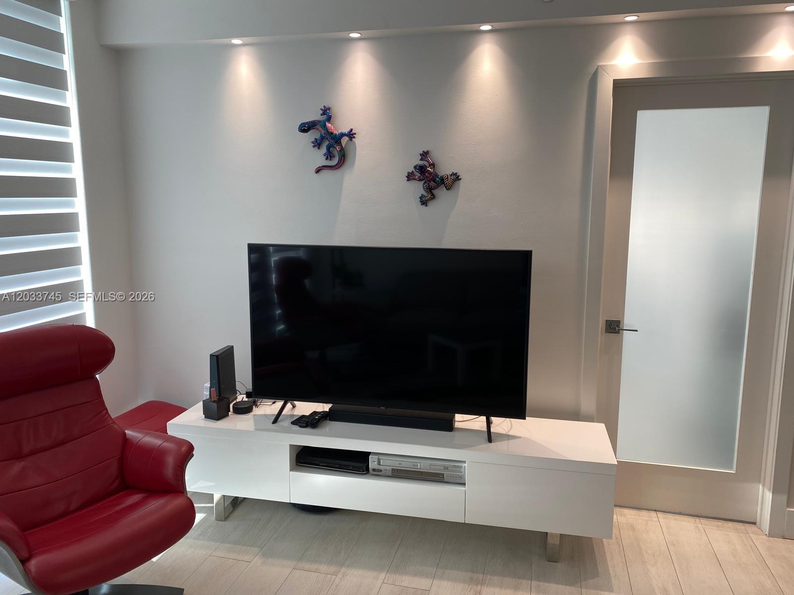 A living room features a television on a white stand with two lizard wall decorations — 5601 Collins Ave # 622, Miami Beach FL 33140, MIAMI BEACH, FL