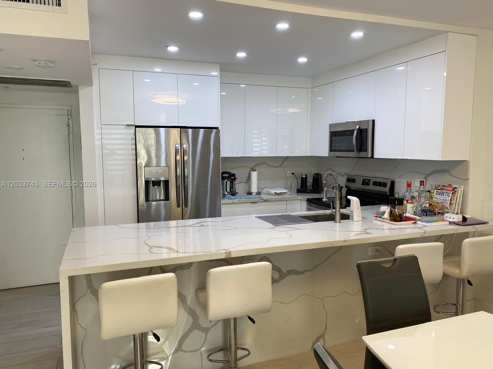 A modern kitchen features white glossy cabinets, stainless steel appliances, and a marble-patterned island countertop — 5601 Collins Ave # 622, Miami Beach FL 33140, MIAMI BEACH, FL