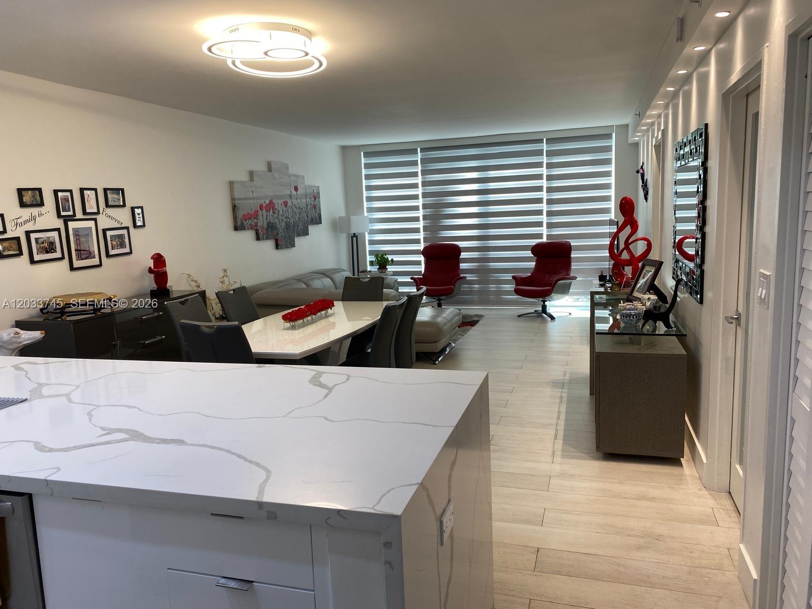 A modern open-concept living and dining area features white marble countertops, tile flooring, and red accents — 5601 Collins Ave # 622, Miami Beach FL 33140, MIAMI BEACH, FL