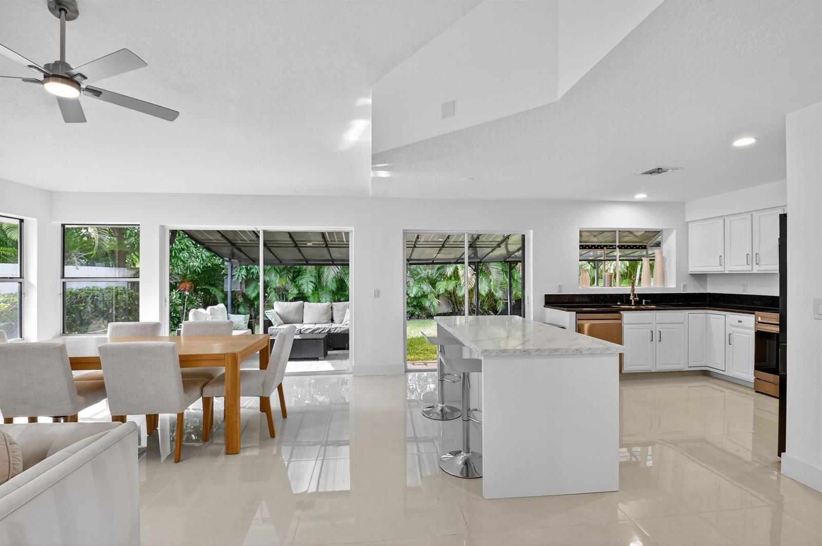 A bright, open-concept kitchen and dining area features white cabinetry, a marble-topped island, and sliding glass doors — 2218 NW 52nd Street, Boca Raton FL 33496, BOCA RATON, FL