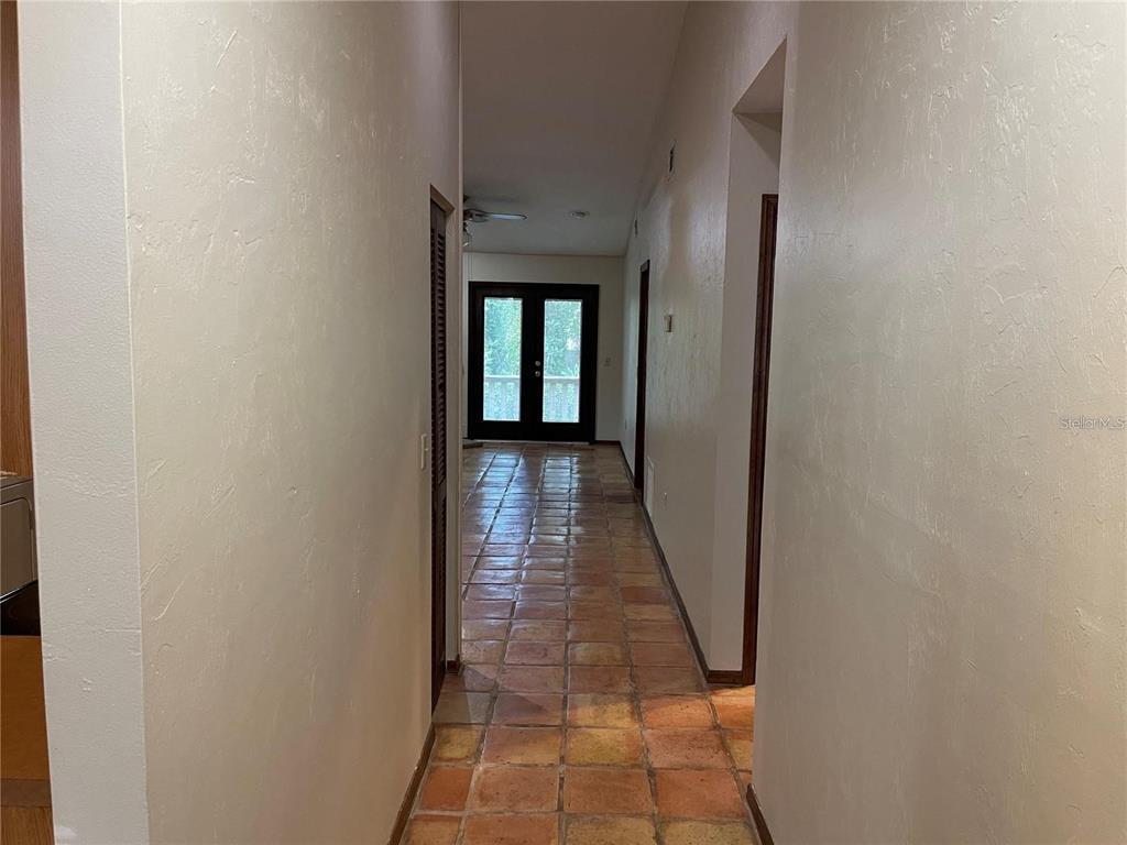 A hallway with terracotta tile flooring leads to a set of dark-framed French doors — 5213 SW 92ND COURT, GAINESVILLE, FL
