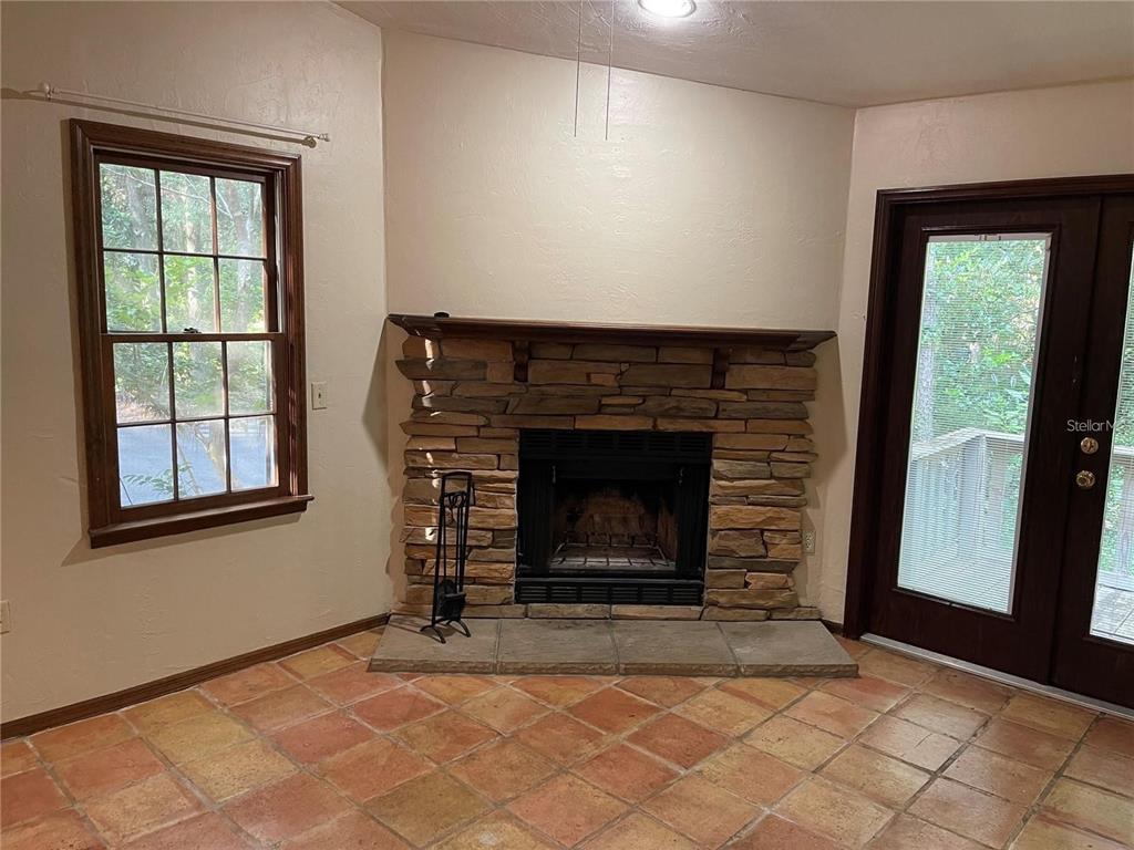 A room with terracotta tile flooring, a stone fireplace, a window, and a glass door — 5213 SW 92ND COURT, GAINESVILLE, FL