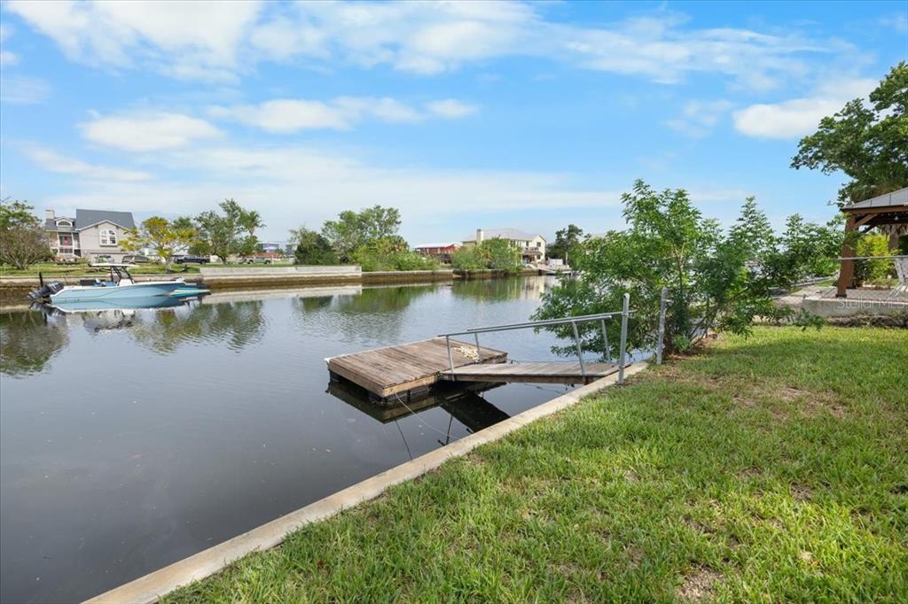 A wooden floating dock sits in a canal next to a grassy lawn — 3478 COMPANERO ENTRA, HERNANDO BEACH, FL