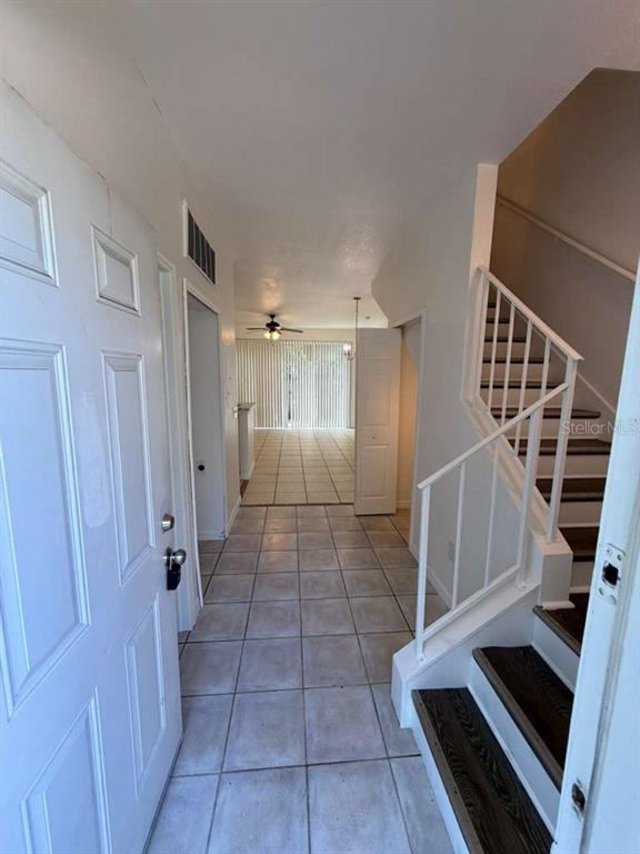 An entryway features tile flooring, a staircase with dark treads, and a view toward sliding doors — 4478 SAINT GEORGES COURT UNIT A, KISSIMMEE, FL
