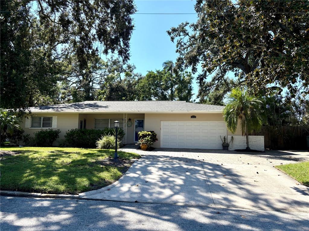 A single-story house with a white garage door, a paved driveway, and mature trees — 1214 21ST STREET W, BRADENTON, FL
