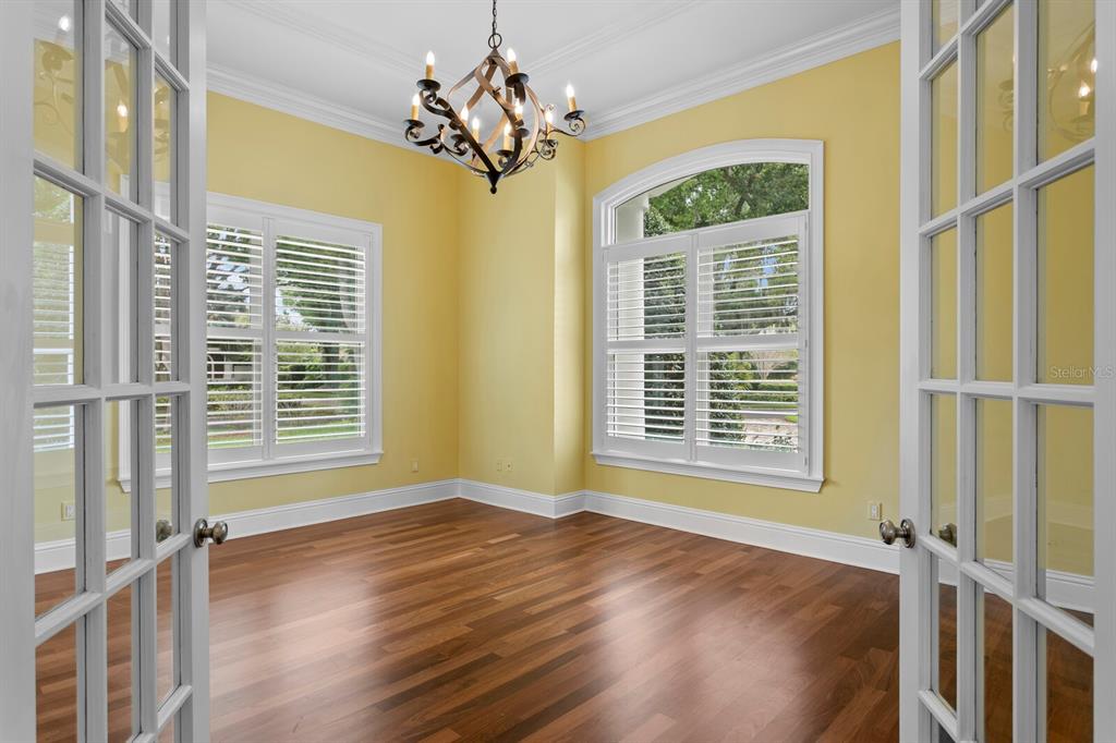 A room with yellow walls, hardwood floors, a chandelier, and windows with white plantation shutters — 16504 AVILA BOULEVARD, TAMPA, FL