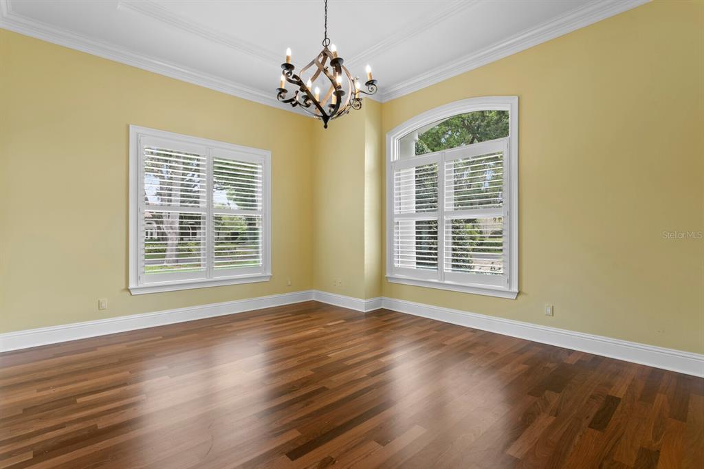 An empty room with yellow walls, hardwood floors, a chandelier, and two shuttered windows — 16504 AVILA BOULEVARD, TAMPA, FL
