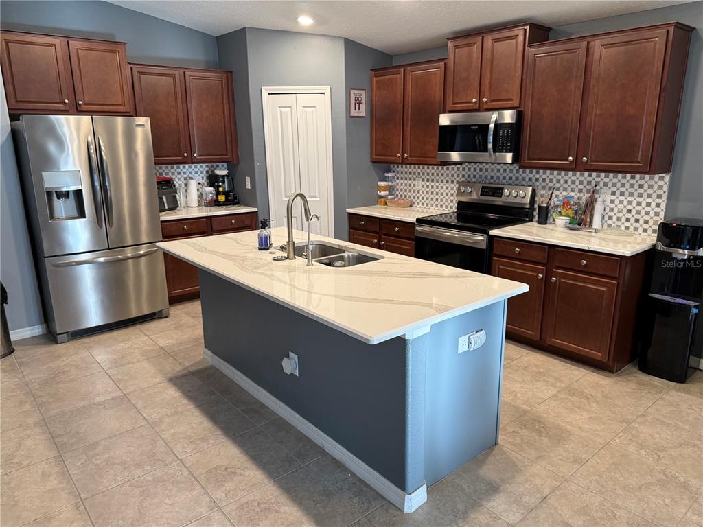 A kitchen features dark wood cabinets, stainless steel appliances, and a central island with quartz countertops — 6629 WAGON TRAIL STREET, ZEPHYRHILLS, FL