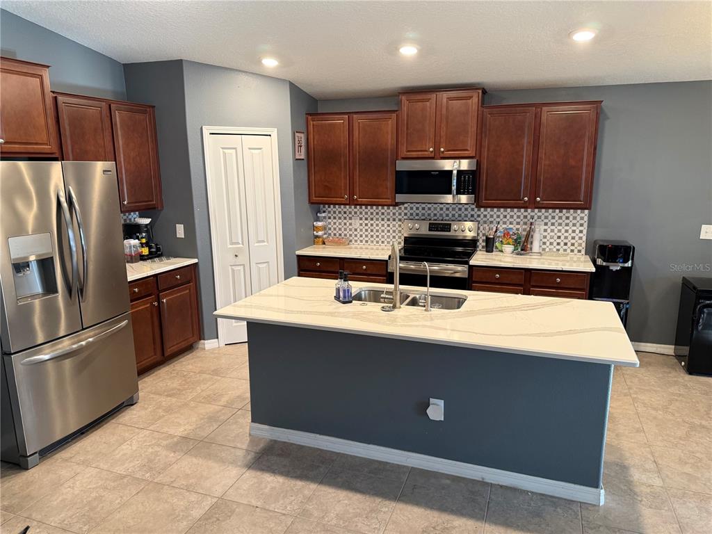 A kitchen features dark wood cabinets, a central island with a white countertop, and stainless appliances — 6629 WAGON TRAIL STREET, ZEPHYRHILLS, FL
