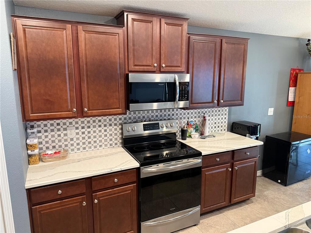 A kitchen features dark wood cabinets, stainless steel appliances, and a patterned tile backsplash — 6629 WAGON TRAIL STREET, ZEPHYRHILLS, FL