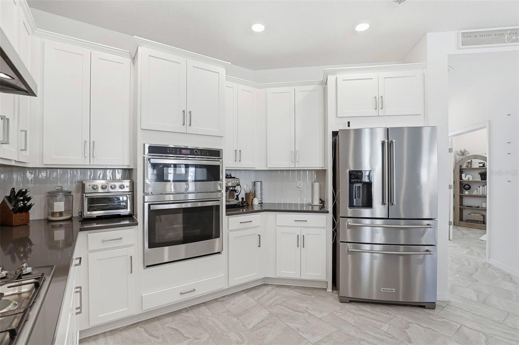 A modern kitchen with white cabinets, stainless steel appliances, and gray tile flooring — 5268 KILDARE PLACE, ST CLOUD, FL