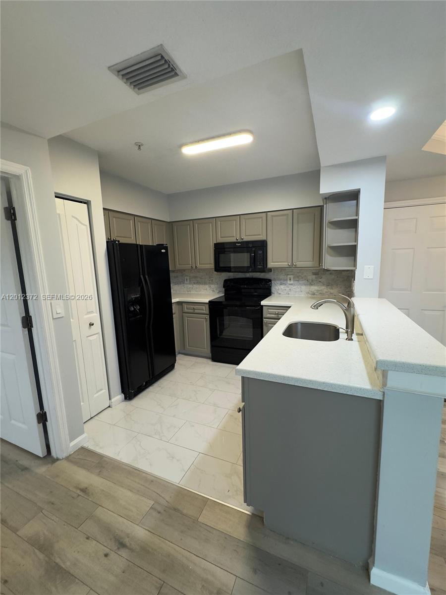 A kitchen features gray cabinets, black appliances, white countertops, and light-colored tile flooring — 2042 Alta Meadows Ln # 1712, Delray Beach FL 33444, DELRAY BEACH, FL