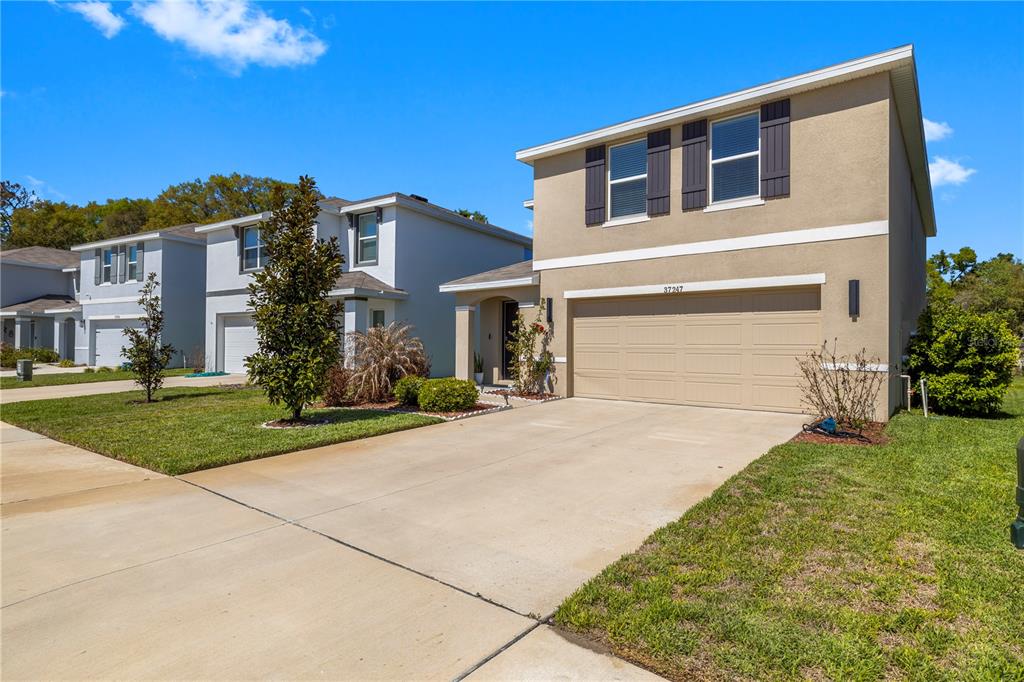 A two-story suburban house with a tan stucco exterior, a two-car garage, and a driveway — 37247 KINGS CROWN DRIVE, ZEPHYRHILLS, FL