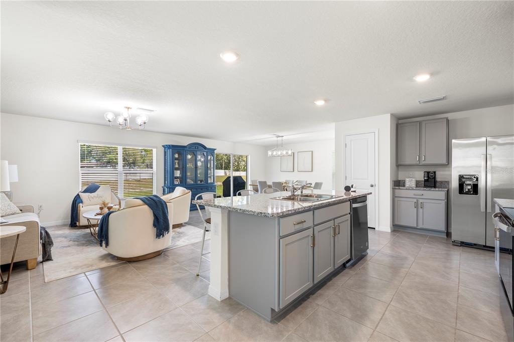 An open-concept kitchen with a granite island, gray cabinetry, and an adjacent living area — 37247 KINGS CROWN DRIVE, ZEPHYRHILLS, FL