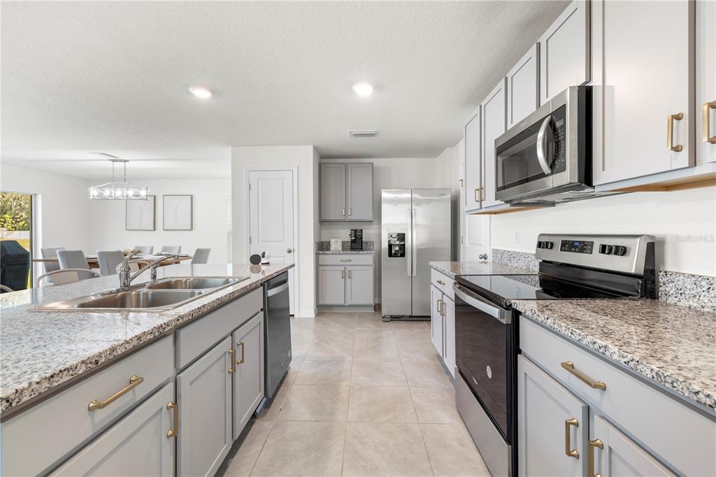 A kitchen with gray cabinets, granite countertops, stainless steel appliances, and a central island — 37247 KINGS CROWN DRIVE, ZEPHYRHILLS, FL