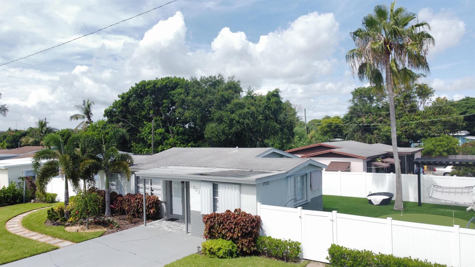 An exterior view of a single-story house with a white fence and a putting green — 702 SW 1st Street, Delray Beach FL 33444, DELRAY BEACH, FL