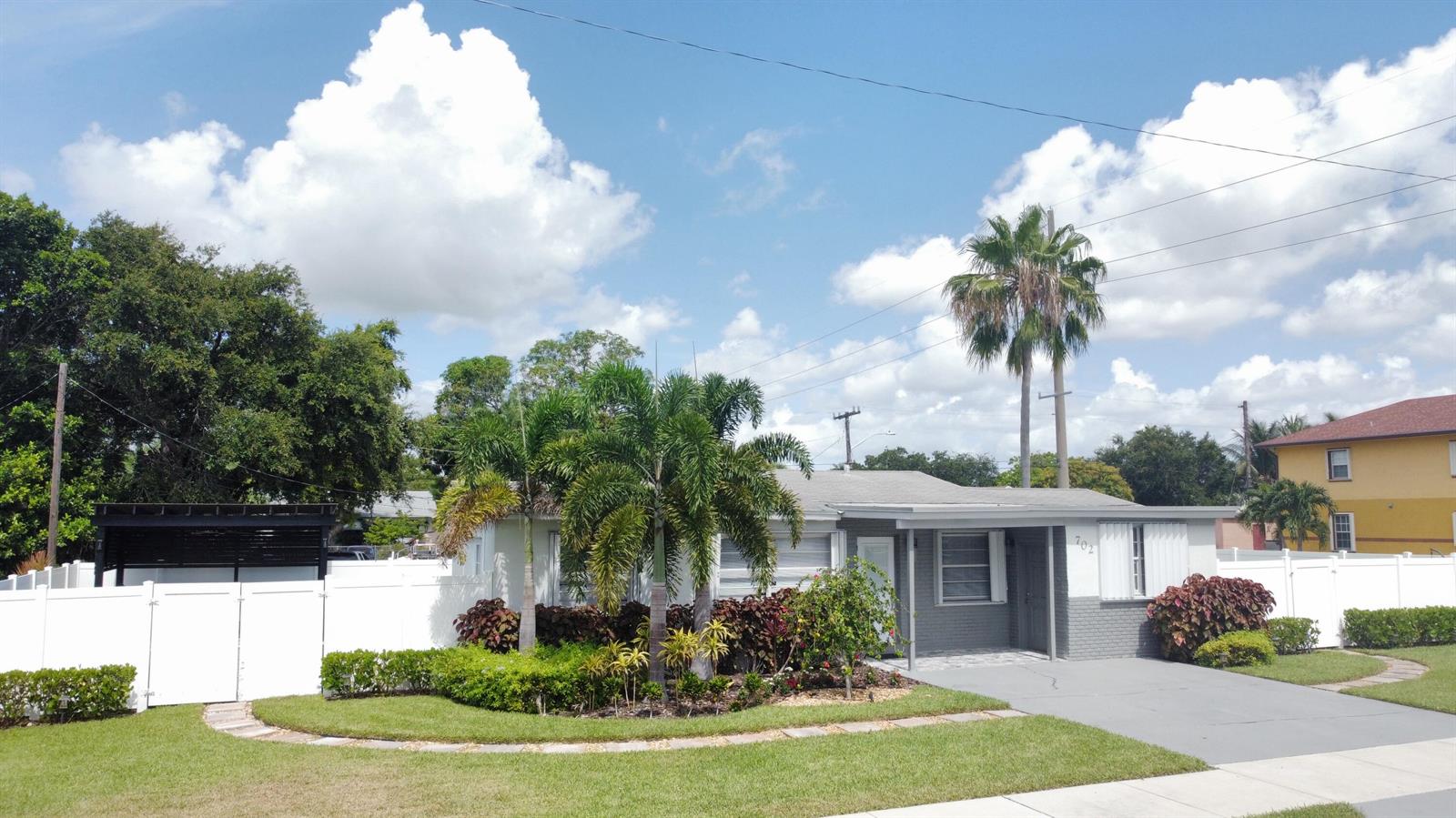 A single-story house with a gray brick facade, palm trees, and a white privacy fence — 702 SW 1st Street, Delray Beach FL 33444, DELRAY BEACH, FL