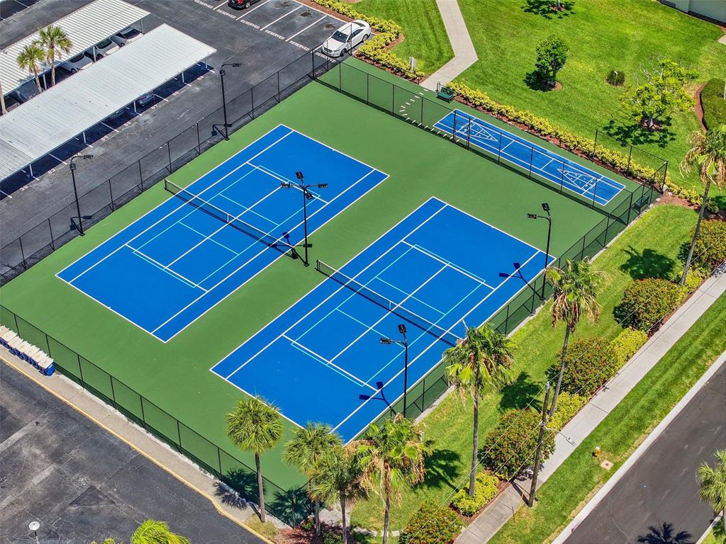 An aerial view shows two blue tennis courts and a shuffleboard court inside a fenced enclosure — 670 ISLAND WAY UNIT 800, CLEARWATER BEACH, FL