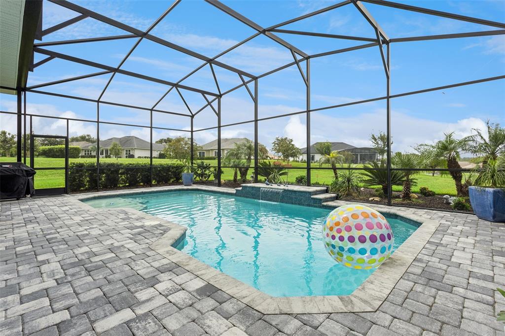 A screened-in swimming pool with a water feature and paver patio overlooks a grassy yard — 5141 GREENS DRIVE, LADY LAKE, FL