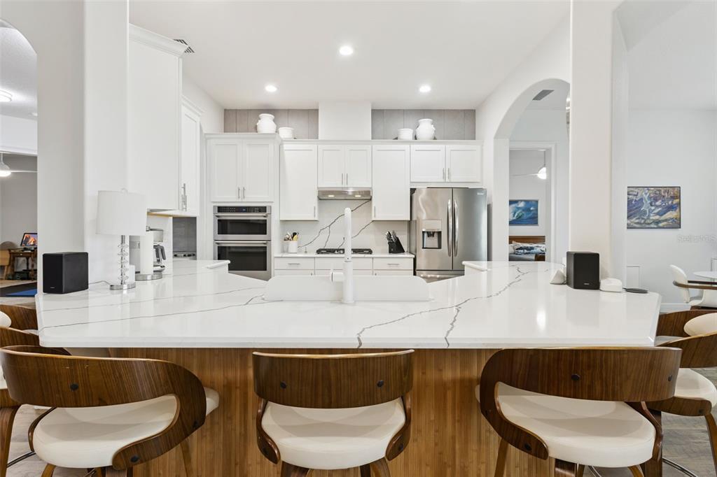 A kitchen features white cabinets, a quartz island with bar seating, and stainless steel appliances — 5141 GREENS DRIVE, LADY LAKE, FL