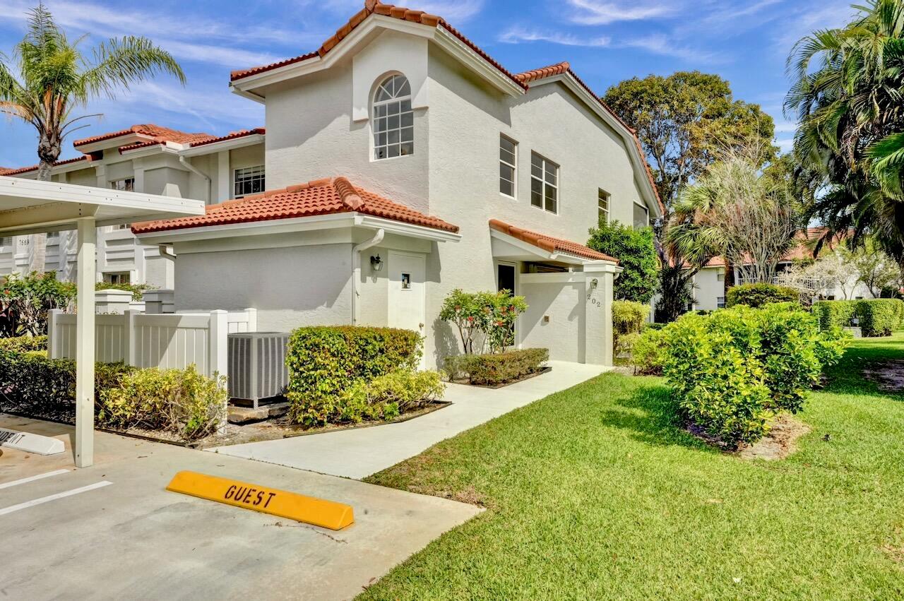 A white stucco townhouse exterior features a front door, a walkway, and lush landscaping — 7669 Springwater Place # 202, Boynton Beach FL 33437, BOYNTON BEACH, FL
