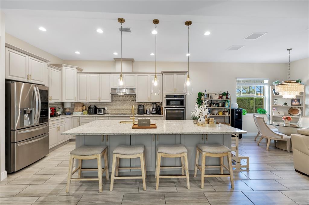 A modern kitchen features light-colored cabinetry, a large granite island with four stools, and stainless appliances — 10720 GAWSWORTH POINT, ORLANDO, FL