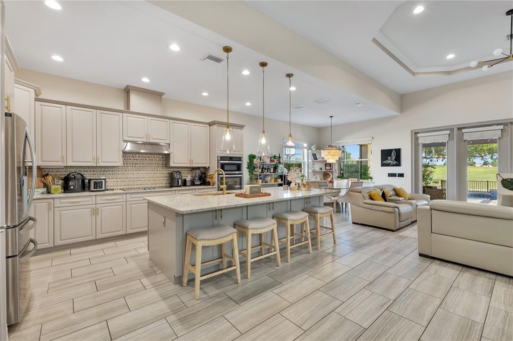 A kitchen with light cabinets, a granite-topped island, and bar stools opens to a living area — 10720 GAWSWORTH POINT, ORLANDO, FL