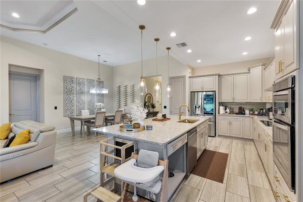 A modern kitchen with light cabinetry, granite countertops, and an island opens to a dining area — 10720 GAWSWORTH POINT, ORLANDO, FL