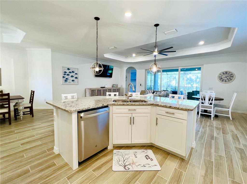 A kitchen island with a stainless steel dishwasher and granite countertop sits in an open-concept room — 14700 CHERRY BLOSSOM WAY, PUNTA GORDA, FL