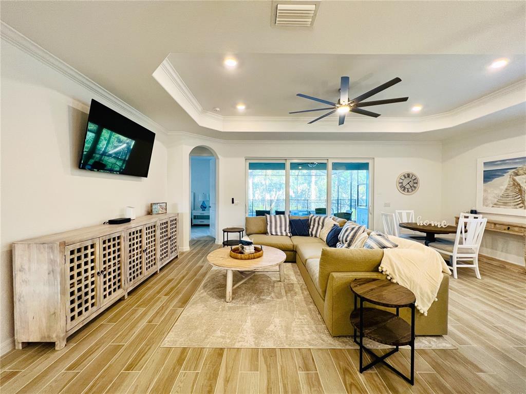 A living room features a sectional sofa, wood-look tile flooring, and a tray ceiling — 14700 CHERRY BLOSSOM WAY, PUNTA GORDA, FL