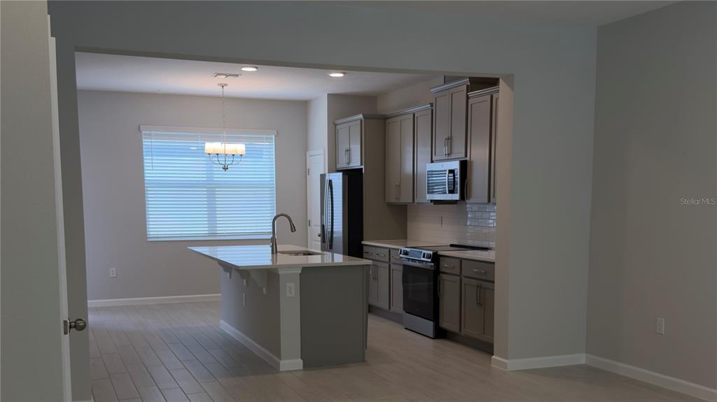 A kitchen features gray cabinets, stainless steel appliances, a center island, and light-colored tile flooring — 438 LADY PALM STREET, APOPKA, FL