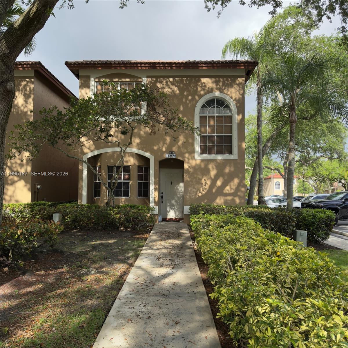 A two-story tan stucco house features a concrete walkway leading to the front entrance — 16029 Emerald Cove Rd, Weston FL 33331, WESTON, FL