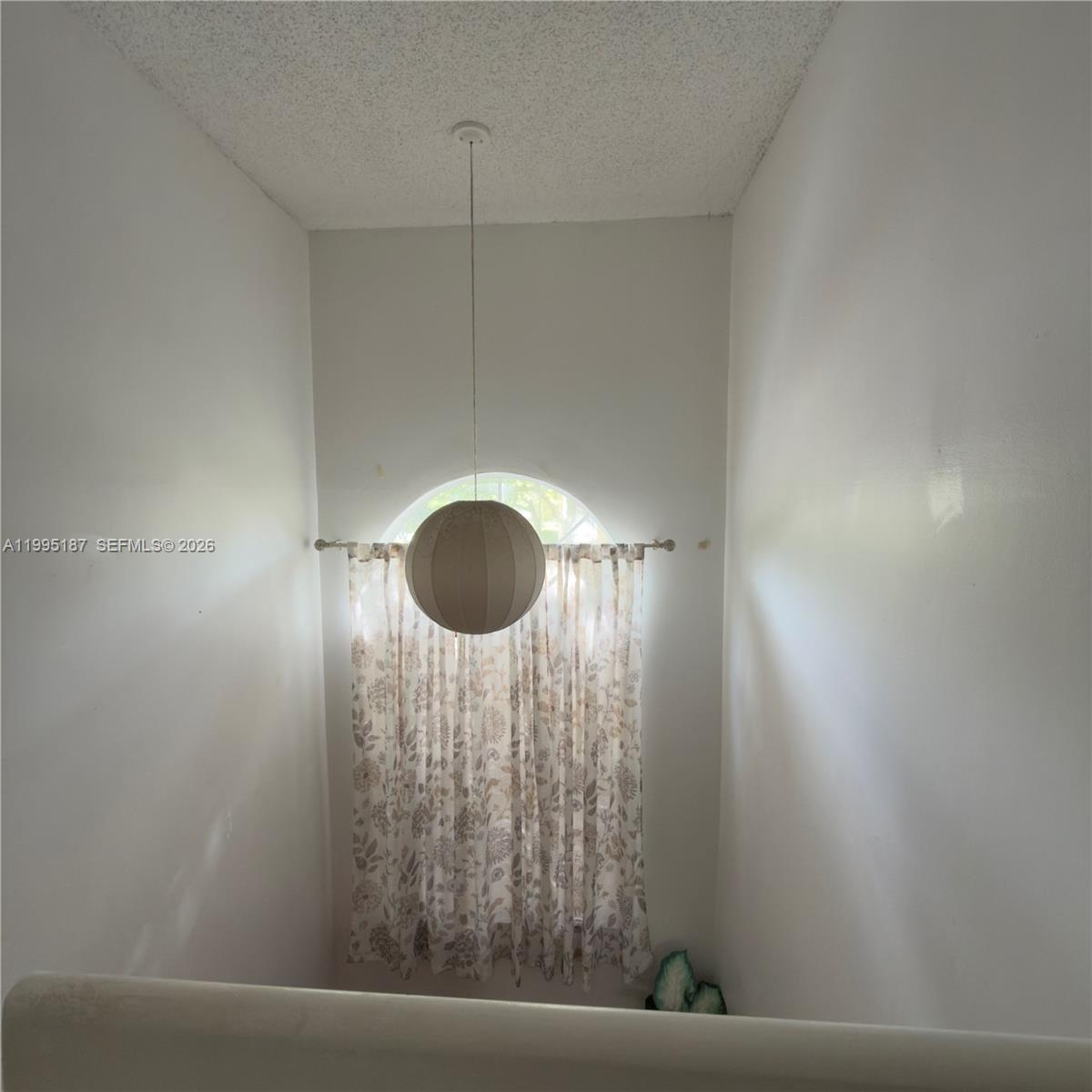 A high-ceilinged stairwell features a round window with floral curtains and a hanging globe pendant — 16029 Emerald Cove Rd, Weston FL 33331, WESTON, FL