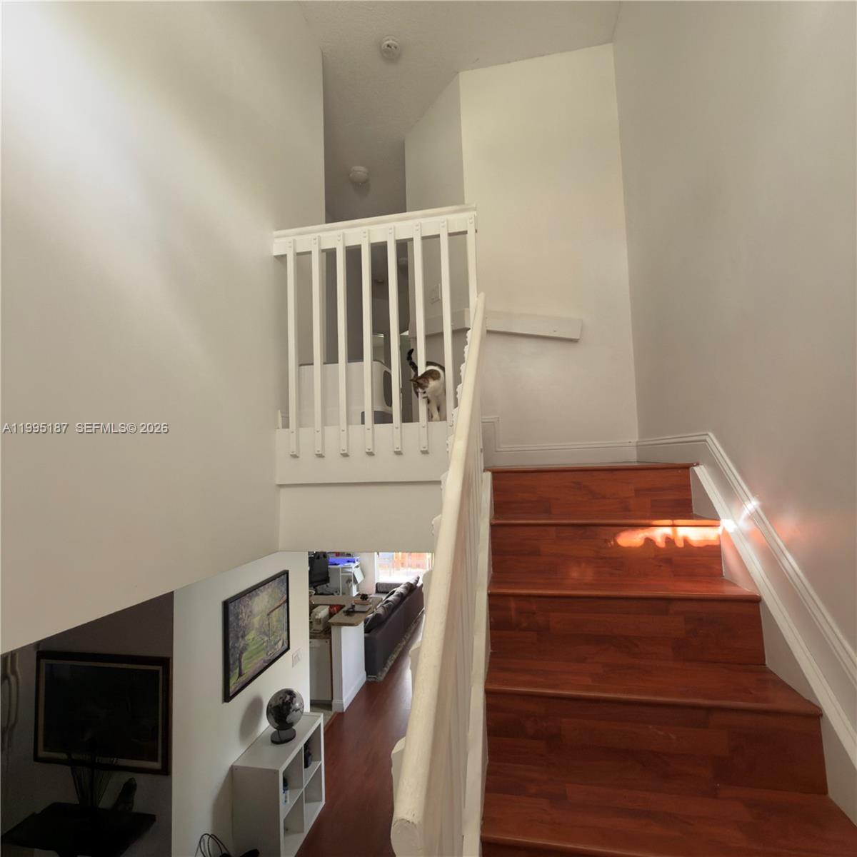 A staircase with wooden treads leads to an upper landing featuring a white railing — 16029 Emerald Cove Rd, Weston FL 33331, WESTON, FL