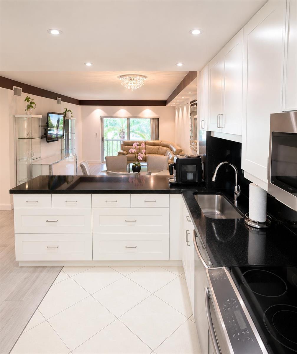A white kitchen with black countertops overlooks a living room with a tan leather sofa — 9880 Marina Boulevard # 1520, Boca Raton FL 33428, BOCA RATON, FL