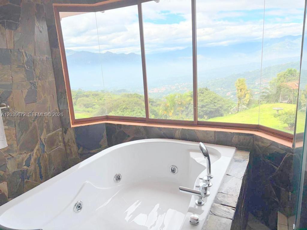 A white soaking tub sits in a stone-walled bathroom with large windows overlooking mountains — NA Via Guadaleg (Ecuador) NA Via Guadaleg (Ecuador), FL