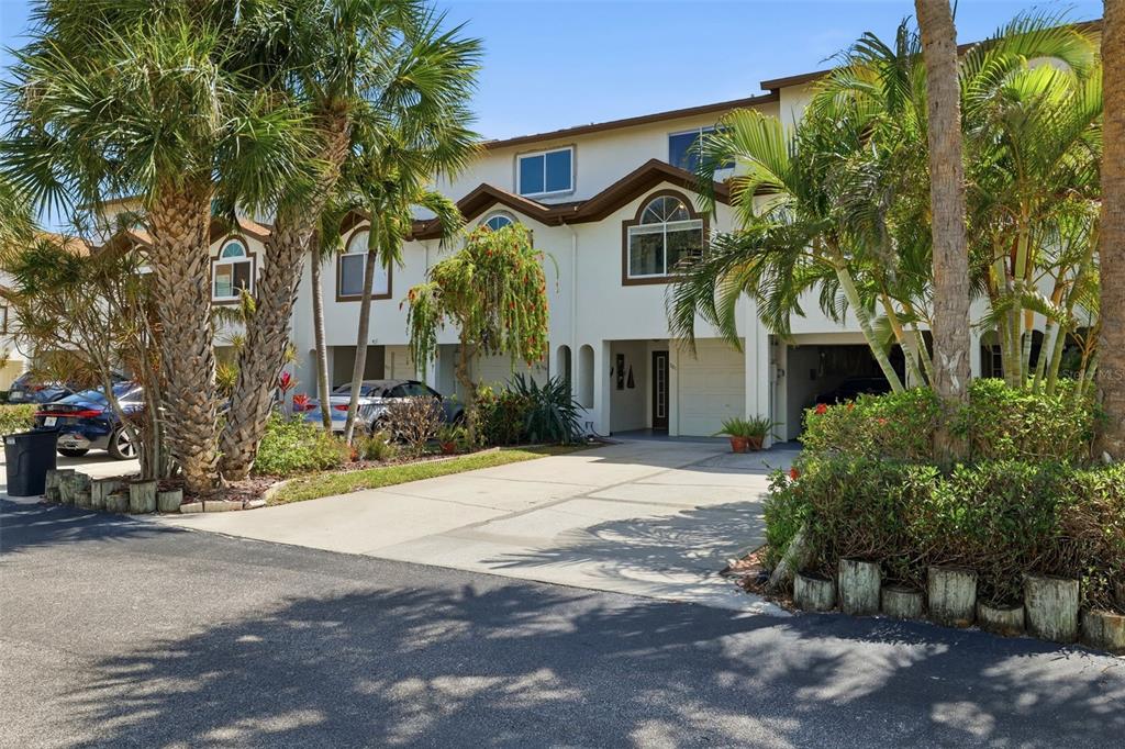 A multi-story townhouse exterior with a concrete driveway, palm trees, and arched windows — 381 MADEIRA CIRCLE, TIERRA VERDE, FL