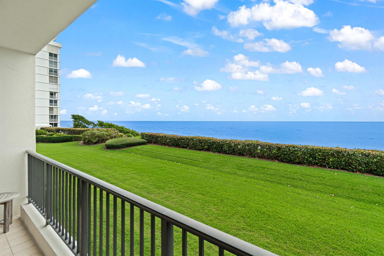 A balcony overlooks a green lawn, manicured hedges, and the blue ocean under a cloudy sky — 800 Ocean Drive # 204, Juno Beach FL 33408, JUNO BEACH, FL