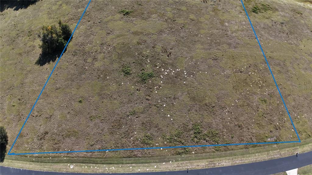 An aerial view shows a vacant, grassy lot outlined in blue next to a paved road — NW 54TH LOOP LOT 7, OCALA, FL