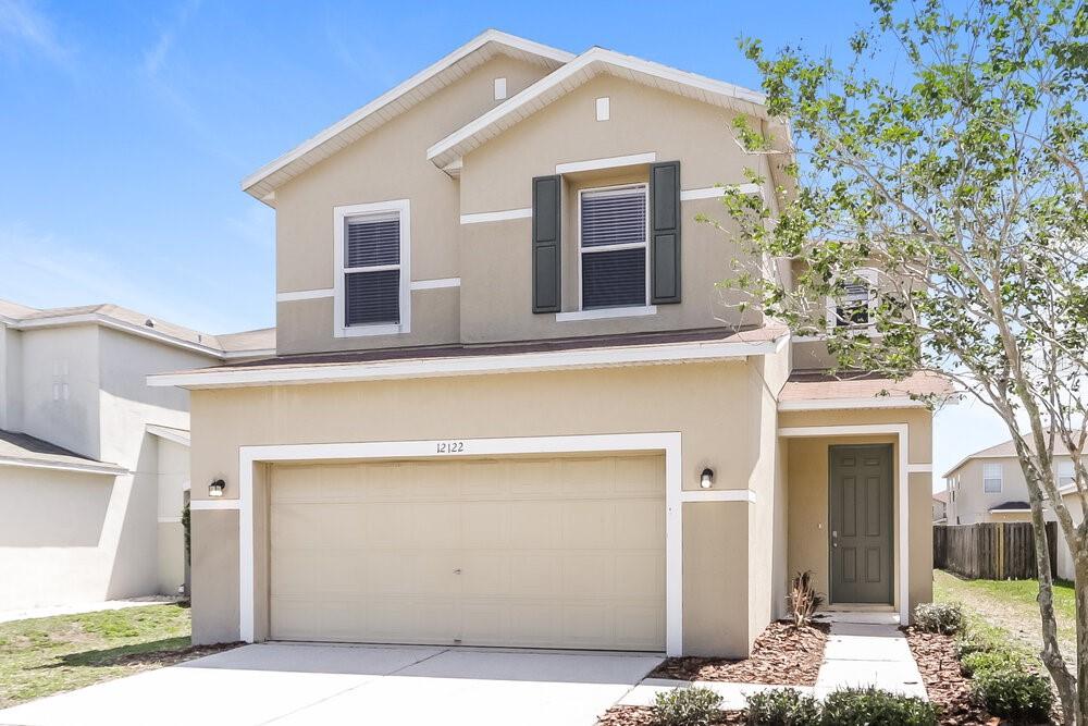 A two-story suburban house with a beige stucco exterior and a two-car garage — 12122 FERN HAVEN AVENUE, GIBSONTON, FL