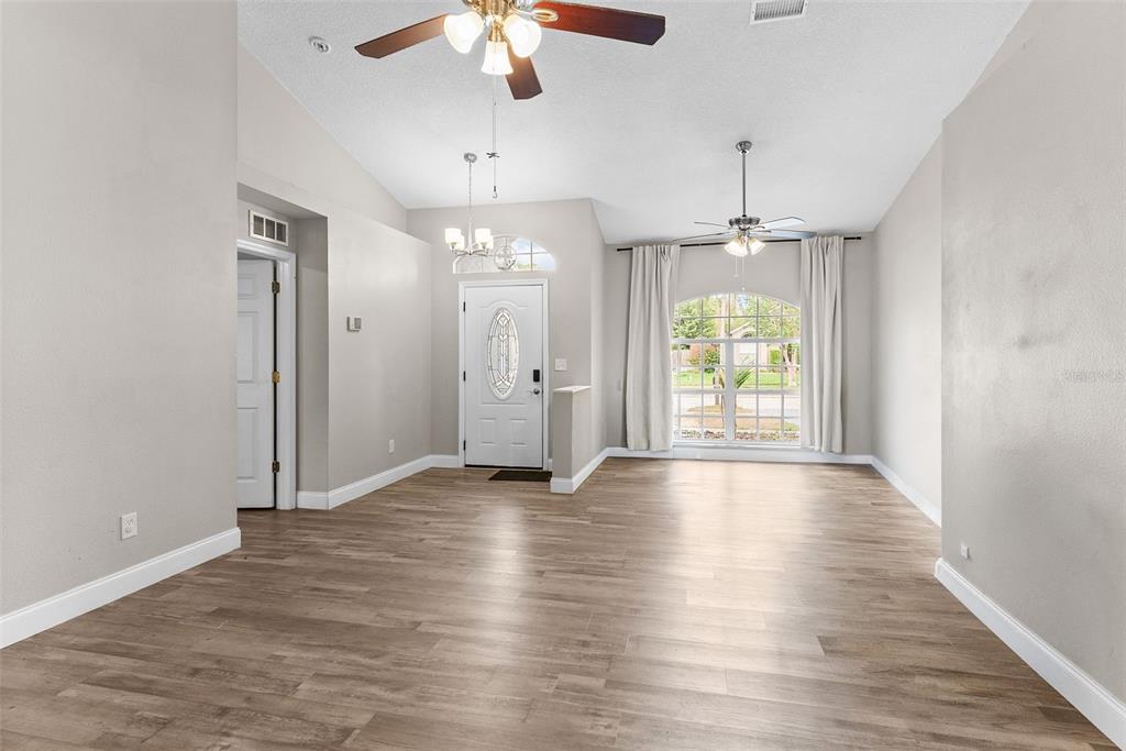 An empty living room with light wood-look flooring, vaulted ceilings, and a white front door — 12106 SHADY FOREST DRIVE, RIVERVIEW, FL