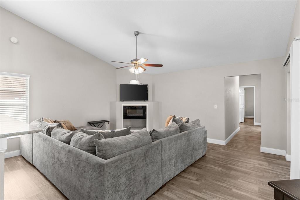 A living room features a gray sectional sofa, a corner fireplace with a television, and wood-look flooring — 12106 SHADY FOREST DRIVE, RIVERVIEW, FL