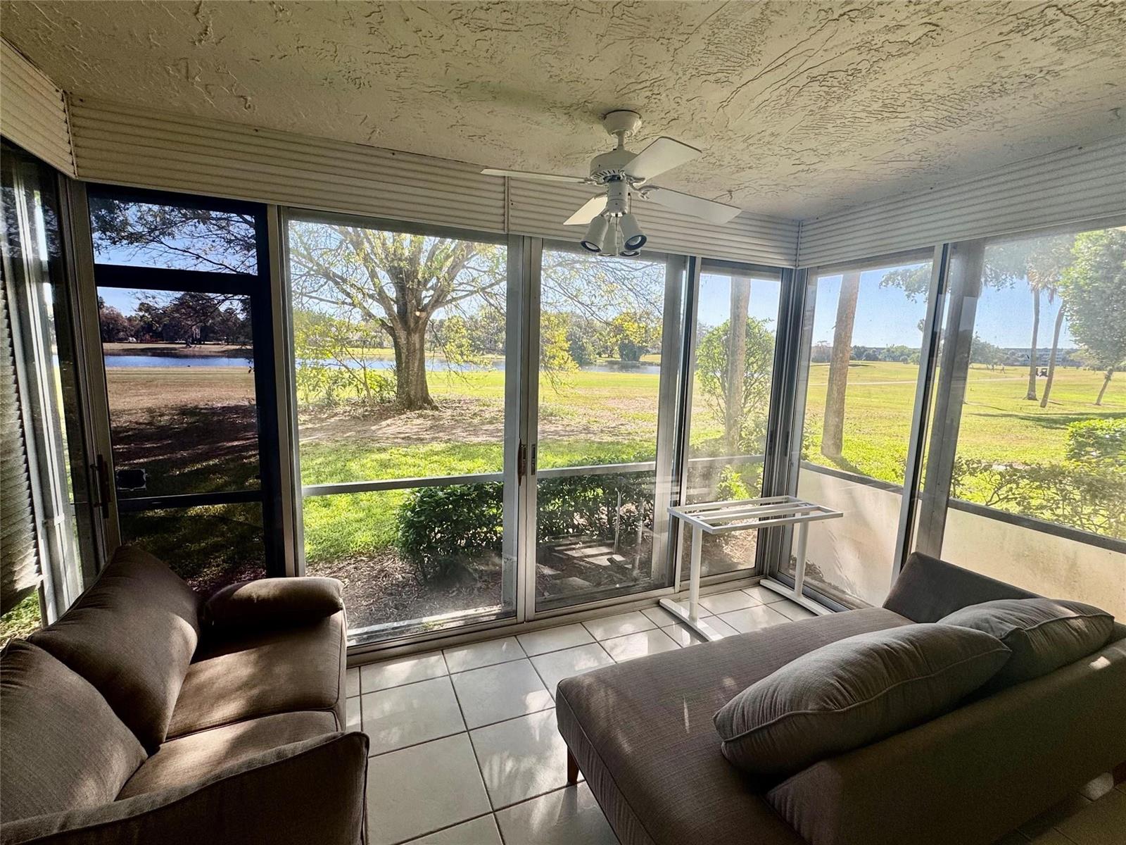 A sunroom with tile floors, two sofas, a ceiling fan, and large windows overlooking a golf course — 804 Cypress Boulevard # 106, Pompano Beach FL 33069, POMPANO BEACH, FL