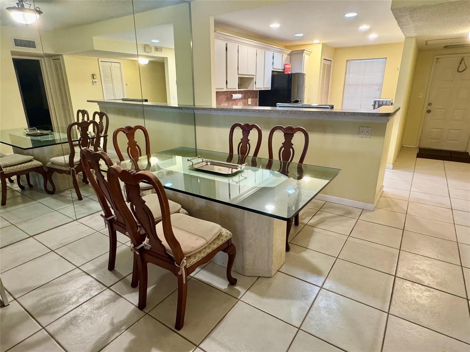 A dining area with a glass-topped table and chairs sits before a kitchen breakfast bar — 804 Cypress Boulevard # 106, Pompano Beach FL 33069, POMPANO BEACH, FL