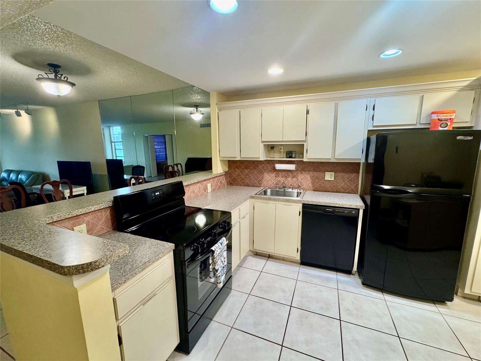 A kitchen features white cabinets, black appliances, granite-look countertops, and a mirrored wall — 804 Cypress Boulevard # 106, Pompano Beach FL 33069, POMPANO BEACH, FL