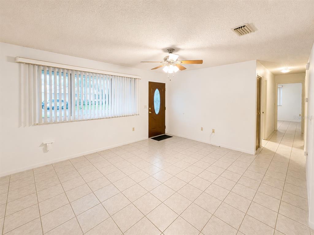 A living room features white tiled floors, a ceiling fan, and a large window with blinds — 8565 SW 109TH STREET, OCALA, FL